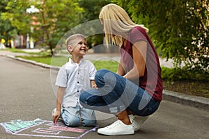 Nanny with cute little boy drawing house with chalks