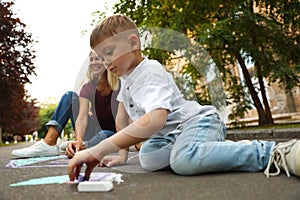 Nanny with cute little boy drawing house with chalks