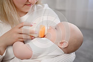 Nanny holds infant in her arms, baby drinks milk from bottle, close-up.Boy or girl drinking formula from a plastic