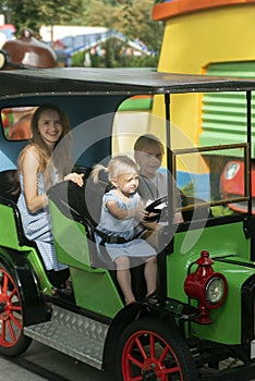 Nanny rides with children in the park. Young mother and two children ride car on an amusement park