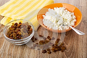 Napkin, bowl with cottage cheese, spoon, bowl with raisin on wooden table