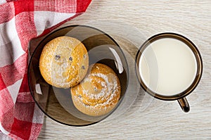 Napkin, cookies with raisin in sugar powder on saucer, glass cup with milk on table. Top view