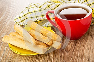 Napkin, cup with tea, salted bread sticks in saucer on wooden table