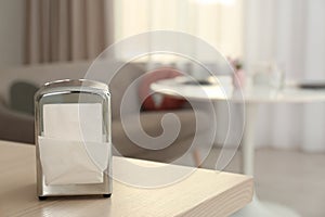 Napkin holder with paper serviettes on table in room.