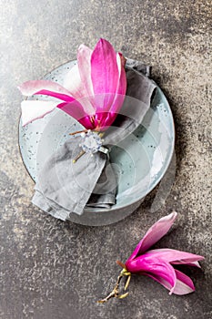 Napkin with srping magnolia flower on gray plate, stone background. Top view