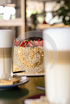 Napoleon cake with fresh strawberries on top served on a white plate with blurred background. Dessert time