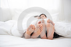 Napping man woman barefoot lying under covers bed hotel room, closer up on couple feet