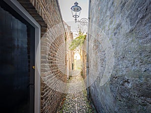 A narrow alley between a building with red brick wall and another with a rough surfaced wall