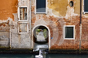 Narrow alley of an old orange building with small bricks and the Venice canal, Italy