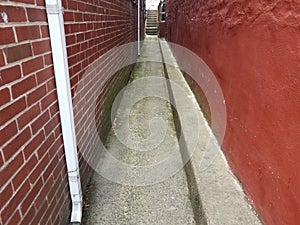 Narrow alley with red wall and bricks on masonry