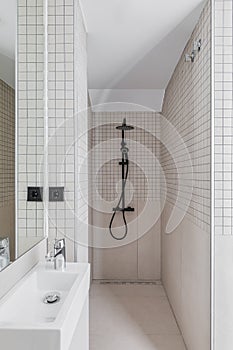 Narrow bathroom with shower zone and small sink. Interior of modern bathroom with beige tiles.