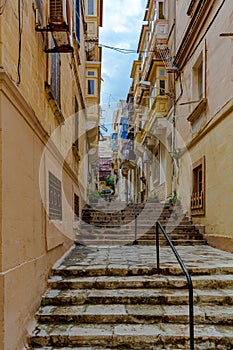 Narrow charming street in Senglea, Malta, with stairs and traditional wooden balconies