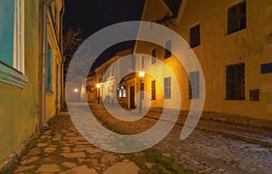 A narrow cobbled street in an old medieval town with lighted houses and antique street lamps. Night shooting