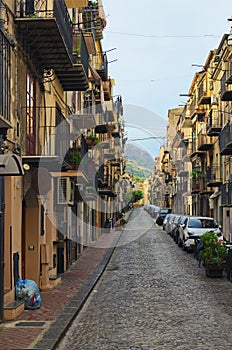 Narrow cobblestone street with densely parked cars. Typical Sicilian street with old residential houses