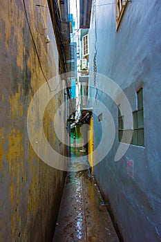 A narrow, colorful, dark alley in between two buildings with open windows and shutters.