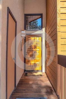 Narrow corridor with shiny brown wood door and transom window at the end