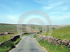 Narrow country lane surrounded by dy stone walls in a sunlit rural hilly landscape on the old howarth road in calderdale west