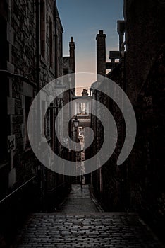 Narrow European alley, surrounded by bricks and cobblestone. Illuminated only with weak light from sunrise. Concept of