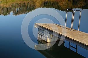A narrow floating wooden jetty in spring on a calm lake with trees in the background