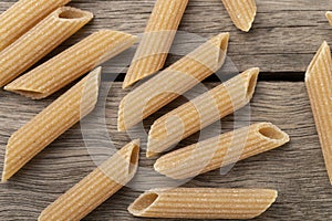 Narrow focus closeup of whole wheat penne pasta over wooden table