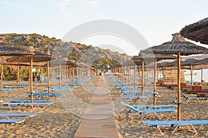 Narrow footpath on the sand surrounded by sunloungers and thatched umbrellas.