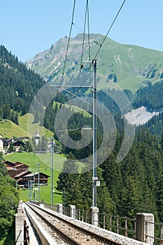 Narrow gauge railroad tracks lead over a long bridge in the Swiss Alps near Arosa