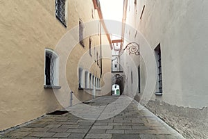 Narrow inner paved stone urban street road passage in old european city. Vintage dark alley with lamp lantern and grey