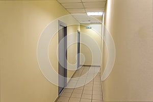 A narrow light corridor in the office room with a few gray doors