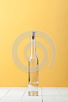 A narrow long glass bottle on a light white and yellow background