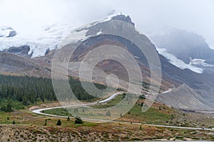 A narrow road climbing up to the glaciers of Columbia Icefield in Canadian Rockies on a cloudy, rainy day. Peaks with snow caps in