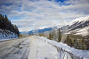Narrow and slippery winter road with big snowbanks curving down from mountain, Banff national park, Canada