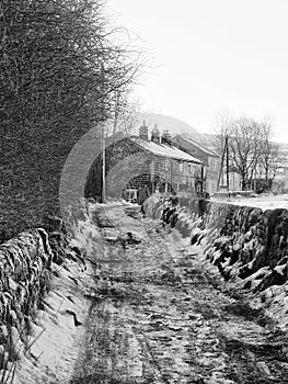 Narrow snow covered country road in rawtenstall near hebden bridge with stone wall and cottages in farmland with the pennine