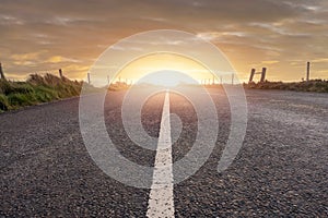 Narrow straight asphalt road with white road markings at sunset. Dramatic sky. Nobody. Low angle of view. Travel concept