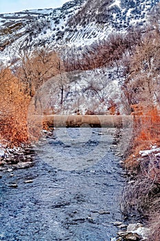 Narrow stream in Provo Canyon with snowy mountain scenery on a cloudy day