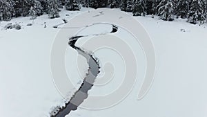 Narrow stream through winter forest landscape, aerial view of snow covered forest