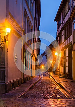 A narrow street along the medieval half-timbered houses in the old town of Quedlinburg illuminated by the warm light of the lamps