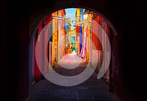 Narrow street with blue, red, green and purple house facade in the island of Burano, Venice