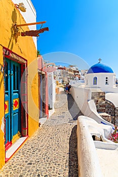 Narrow street with colourful house and church in Oia village, Santorini island, Greece