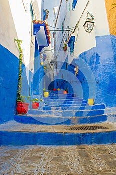 A narrow street in the old medina of Chefchaouen in Morocco, painted blue, with colourful planters.