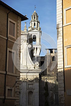 Narrow street of Rome and white church with bells