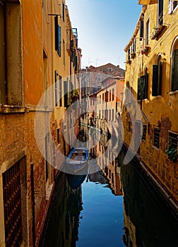 Narrow street in Venezia historical town with canal and boat, blue water and old yellow buildings in Italy