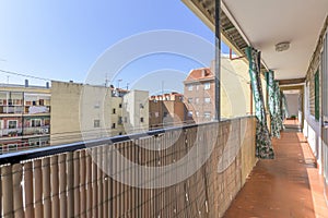 Narrow terrace balcony for access to homes with metal railing and green extendable curtains inside a block patio