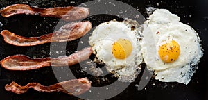 Narrow view of bacon and eggs frying on a cast iron griddle pan.