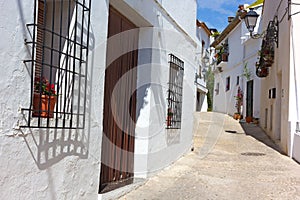 A narrow winding street with residential houses painted in white color and decorated by plants in Althea, Spain.