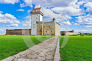 Narva medieval castle with its stone walls and its access road in the green meadow,