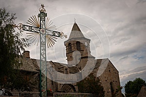 Nasbinals church with ornamental  cross in forground , cloudy skys , Lozere ,France