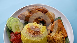 Nasi Kuning or Yellow rice with traditional fried chicken, tofu, tempeh, and smashed potato on blue background.