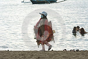 Nasugbu, Batangas, Philippines - Mar 2021: A local woman wearing a face mask walks around the beach selling trinkets and souvenirs