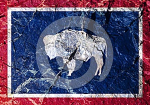 National flag of American state Wyoming on blue with a red border painted on mountain wall. In center is silhouette white bison