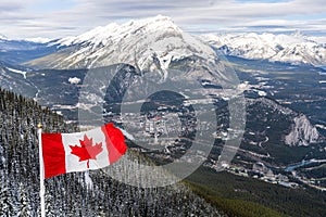 National Flag of Canada with Town of Banff, surrounding snow-covered Canadian Rocky Mountains in winter. Banff National Park